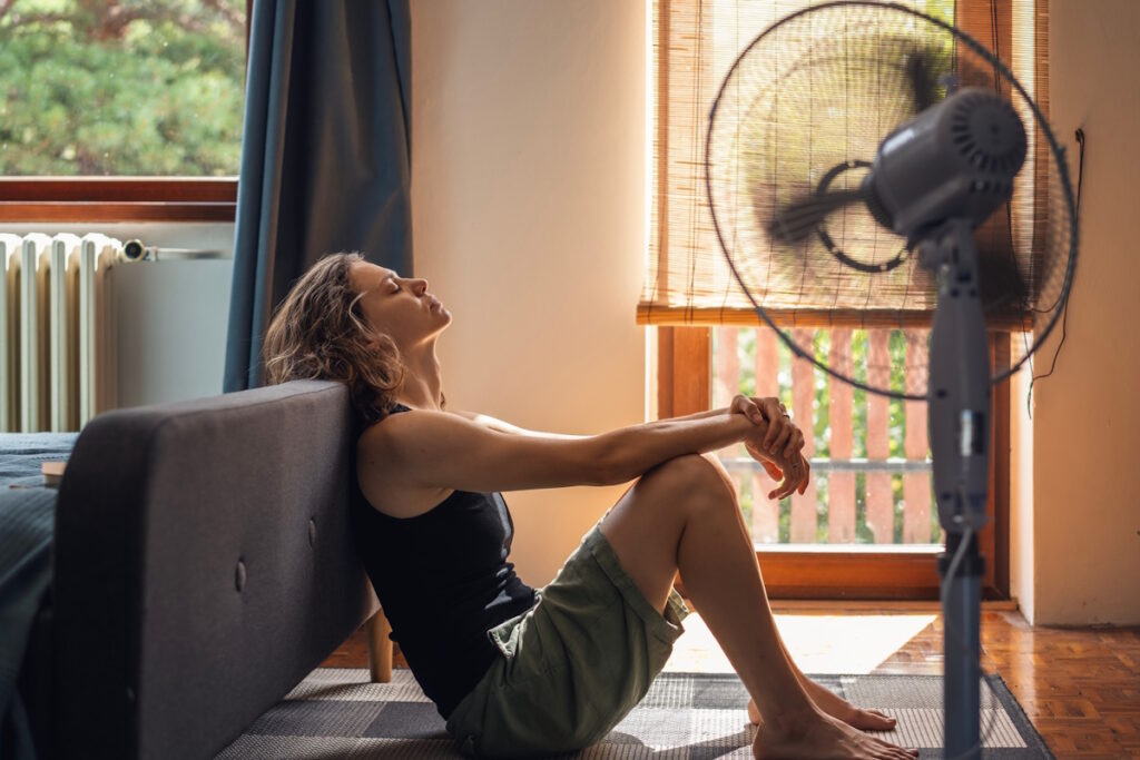 woman cooling off in front of fan in a house with a broken ac